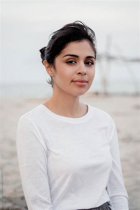 Portrait Of Brunette Woman Wearing White Shirt At The Beach Del Colaborador De Stocksy