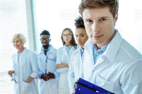 Young doctor in lab coat holding clipboard with group of young doctors ...