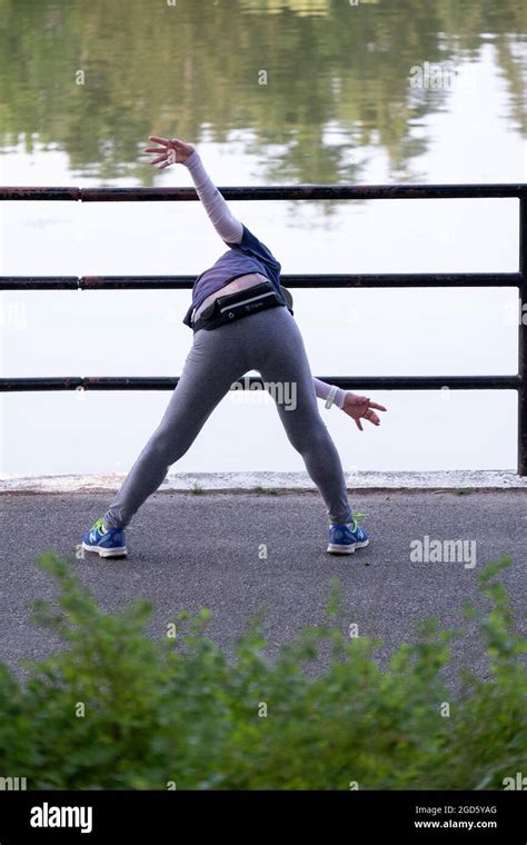 An Unidentified Woman In Her 60s Bends At The Waist And Rotates Her Arms Near The Lake In