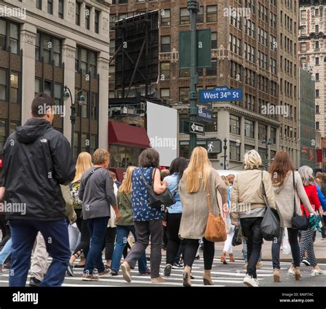 People Walk Across A Busy Manhattan Crosswalk In New York City During