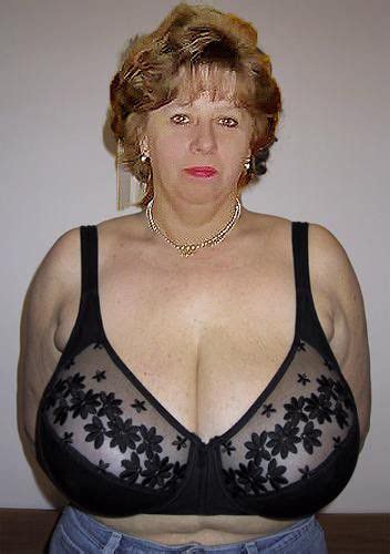 A Woman With Very Large Breast Standing In Front Of A White Wall Wearing Jeans And A Black Bra