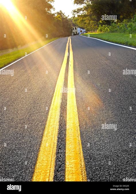 Brilliant Rays Of Late Day Sunlight Glow Across A Long Road Through The