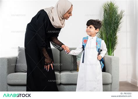 طفل عربي خليجي سعودي يرتدي حقيبة الظهر المدرسية، ارتداء الزي المدرسي، أم تمسك بيد طفلها