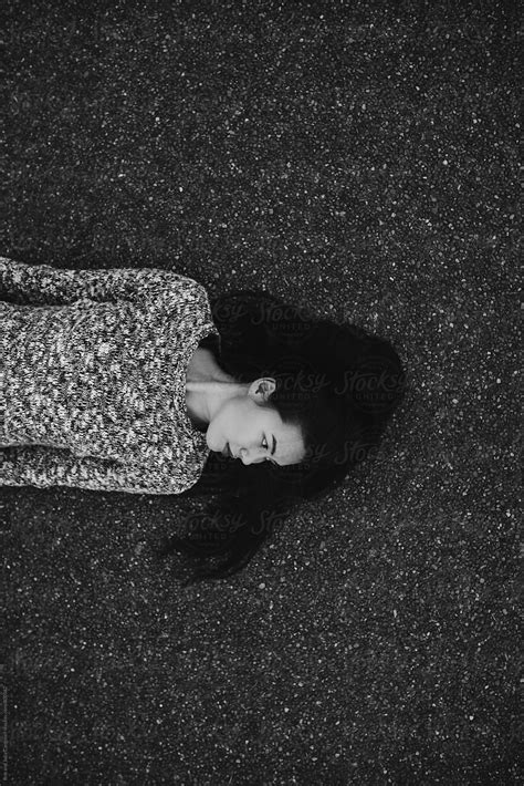 Young Black Haired Woman Lying Down On Sidewalk By Stocksy