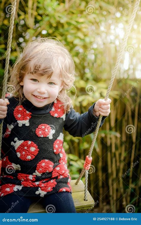 Beautiful Little Girl Playing On Her Swing In The Garden Stock Photo