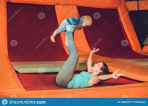 Mother And Her Son Jumping On A Trampoline In Fitness Park And Doing Exersice Indoors Stock