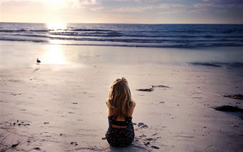Девушка сидит на песке и смотрит на птицу обои для рабочего стола