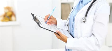 Close Up Of A Female Doctor Filling Up Medical Form At Clipboard While