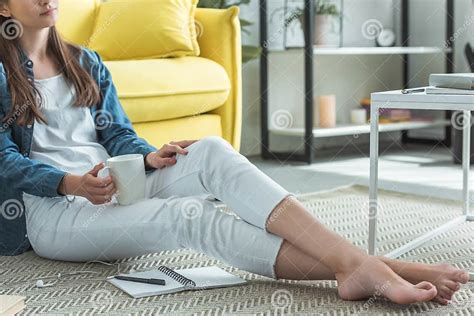 Cropped Shot Of Barefoot Girl Holding Cup While Sitting On Carpet And