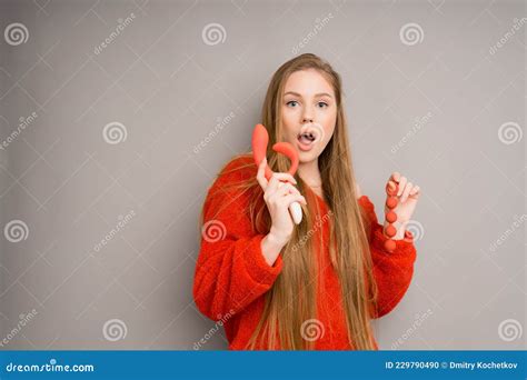 an attractive girl in a sweater is surprised opening her mouth holding a red dildo vaginal