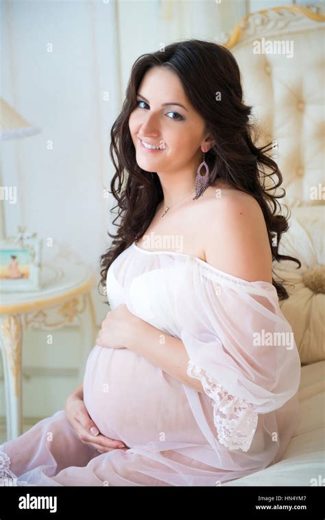 beautiful pregnant girl in a lace negligee sitting on a bed of roses and touching hair stock