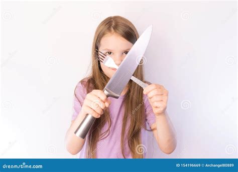 Little Cute Girl Holding A Knife And Fork Crosswise On A Light