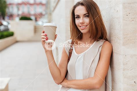 happy woman holding take away coffee and looking at camera while standing on the street royalty