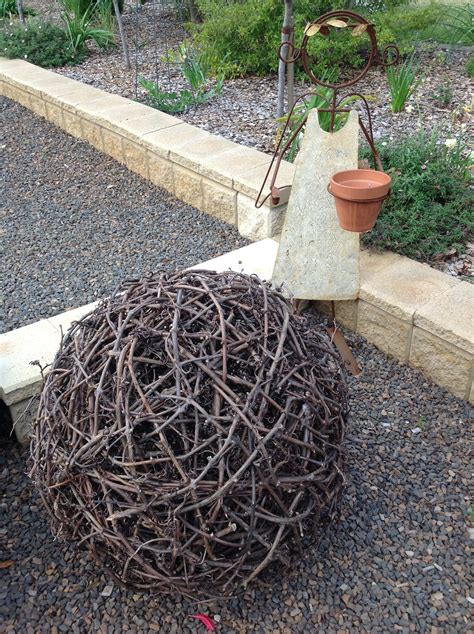 A Large Ball Of Twigs Sitting On Top Of A Gravel Ground Next To A Planter