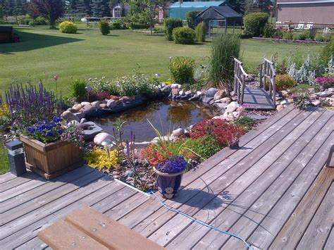 A Wooden Deck Surrounded By Flowers And Plants Next To A Small Pond In