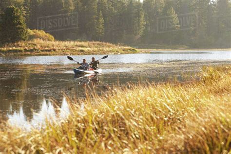Two Young Men Kayaking On A Lake Tall Grass In Foreground Stock