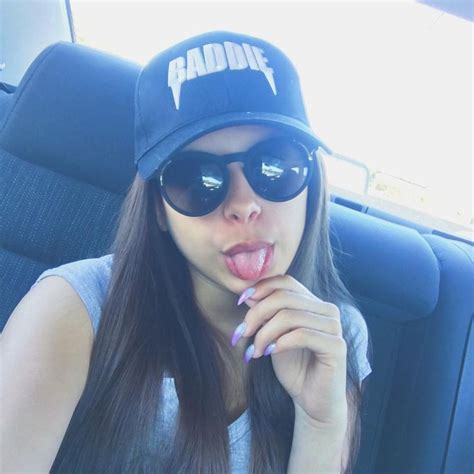 A Woman Sticking Her Tongue Out In The Back Seat Of A Car While Wearing Sunglasses And A Hat