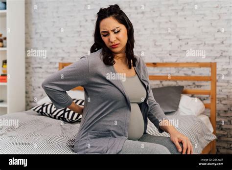 Asian Mixed Caucasian Pregnant Woman Suffering Back Pain Sits On Bed At