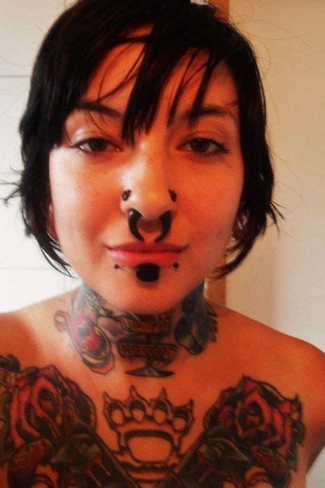 A Woman With Tattoos And Piercings On Her Chest Is Looking At The Camera While Wearing A Fake