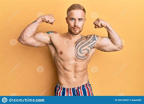 jeune homme caucasien portant des maillots de bain torse nu montrant bras muscles sourire fier