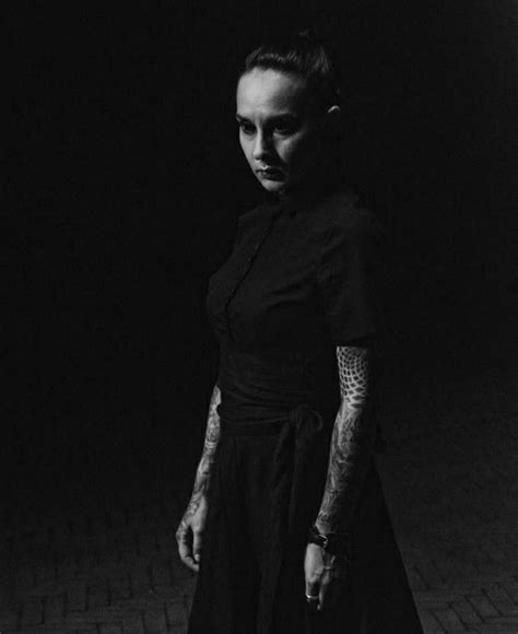 A Woman Standing In The Dark With Tattoos On Her Arm And Arms Wearing