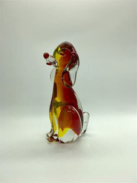 A Glass Dog Figurine Sitting On Top Of A White Table Next To A Red And
