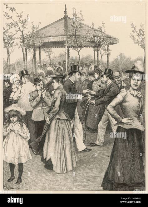 A Crowd Of People Of All Ages Enjoy Themselves By The Bandstand In