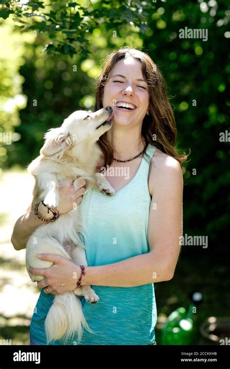 Cheerful Young Woman Carrying Playful Dog Licking Her Face In Forest
