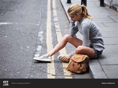 A Young Woman Sits On The Sidewalk In A City Stock Photo Offset