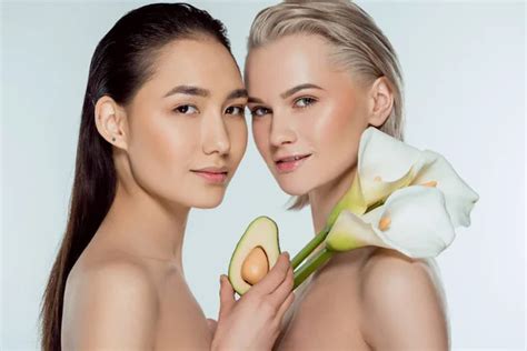 Beautiful Multicultural Naked Girls Posing With Avocado And Calla Flowers Isolated On Grey