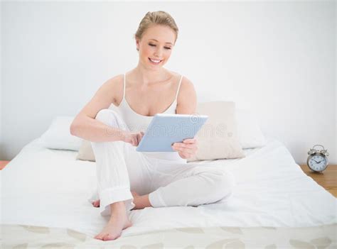 Natural Smiling Blonde Using Tablet While Sitting On Bed Stock Photo