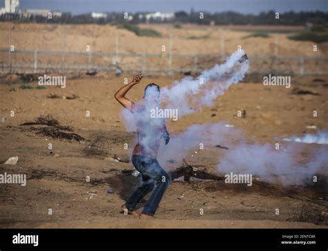 A Palestinian Demonstrator Uses A Slingshot To Throw Back Tear Gas Canisters During An Anti