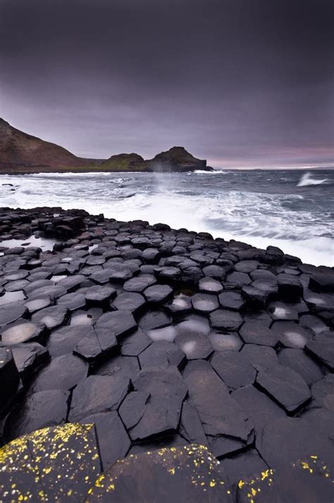 The Giant Rocks Are Covered In Ice As Waves Crash Into The Shore Behind