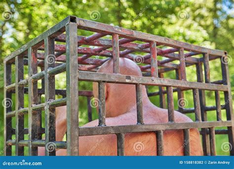 A Bald Man Sits In An Iron Cage Outdoor Filming From Behind Stock