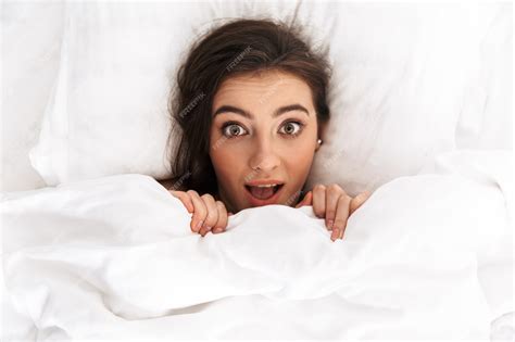premium photo image from top of excited woman 20s with dark hair smiling while lying in bed