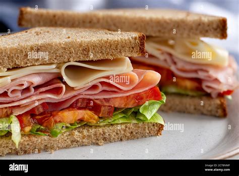 Sandwich With Ham Cheese Lettuce And Tomato On Whole Grain Bread Cut In Half On A Plate Stock