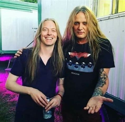 Two Men Standing Next To Each Other With Long Hair