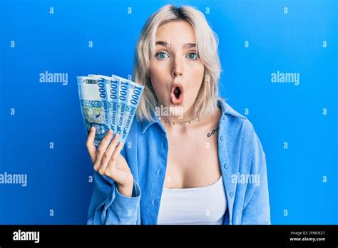 Young Blonde Girl Holding Hungarian Forint Banknotes Scared And Amazed With Open Mouth For
