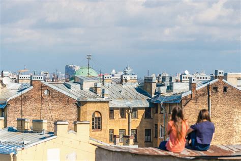 Human Two Women Sitting On Roof Overlooking Building During Daytime
