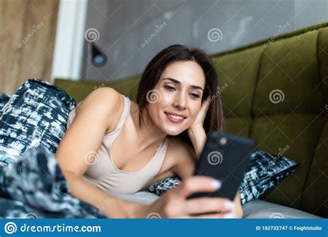 Young Woman Lying In Bed Reaching To Check Mobile Phone Stock Image