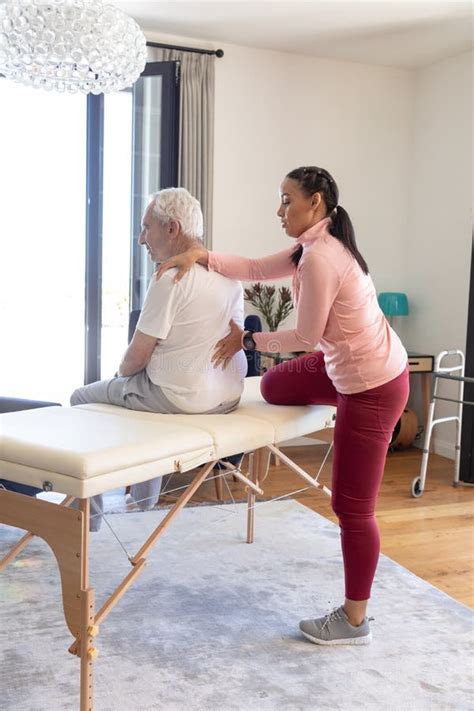 Biracial Female Physiotherapist Giving Back Massage Therapy To Caucasian Senior Man At Home
