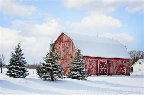 A Red Barn In The Middle Of A Snow Covered Field With Trees On Either Side