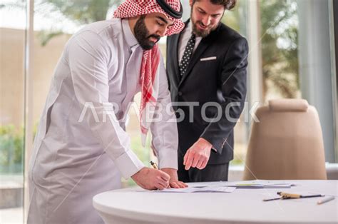 رجل اعمال عربي سعودي خليجي بالثوب السعودي التقليدي يقوم بتوقيع اتفاقية عمل لمشروع جديد مع عميل