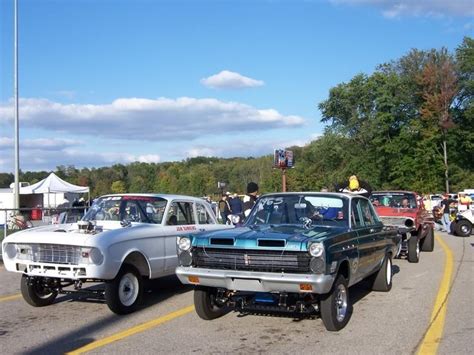 Several Classic Cars Are Parked On The Side Of The Road As People Watch