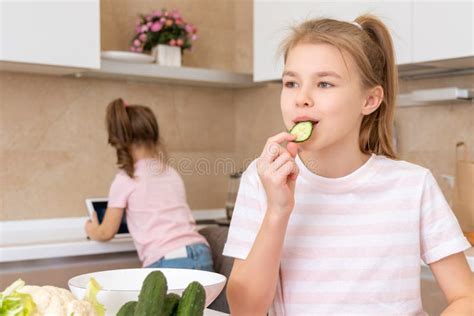 Preteen Girl Cutting And Eating Cucumber With Knife On A Table In