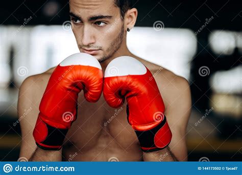 Sportsman With A Naked Torso Keeps His Hands In The Red Boxing Gloves Next To His Face In The