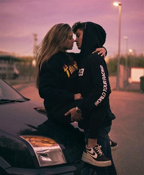 A Man And Woman Kissing On The Hood Of A Car In Front Of A Parking Lot