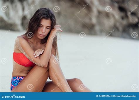 Slender Tanned Woman In Colored Swimsuit Relaxes On Beach With White