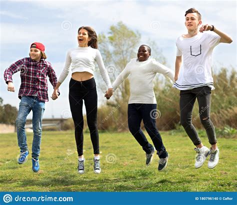 Teenagers Running Jumping Green Lawn In Summer In Park Stock Photo