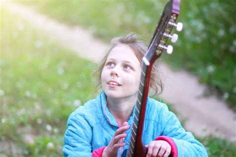 Little Girl Playing Guitar And Singing Outdoors On Green Meadow At